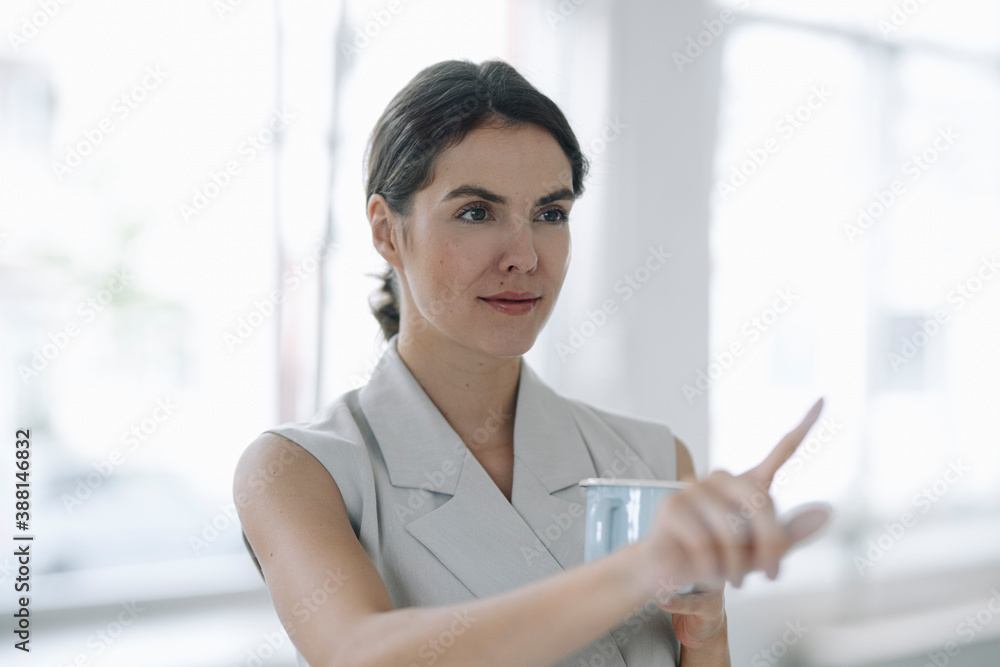 Young woman pointing at glass wall while standing at office Young woman pointing at glass wall while standing at office