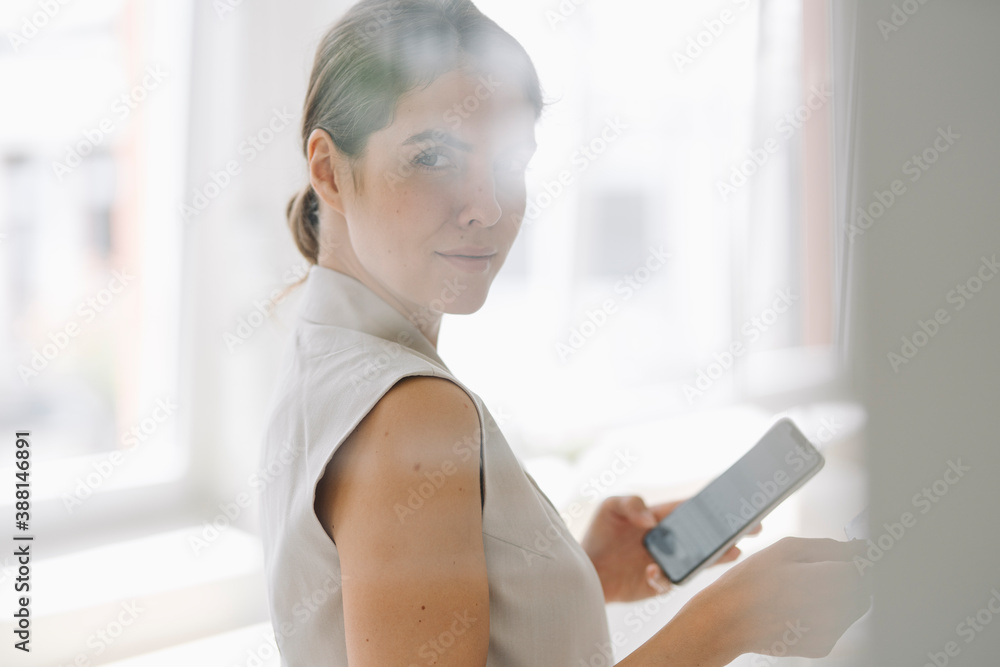 Confident businesswoman using phone while standing at office Confident businesswoman using phone while standing at office