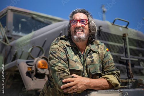 Smiling army soldier with arms crossed leaning on military truck during sunny day photo