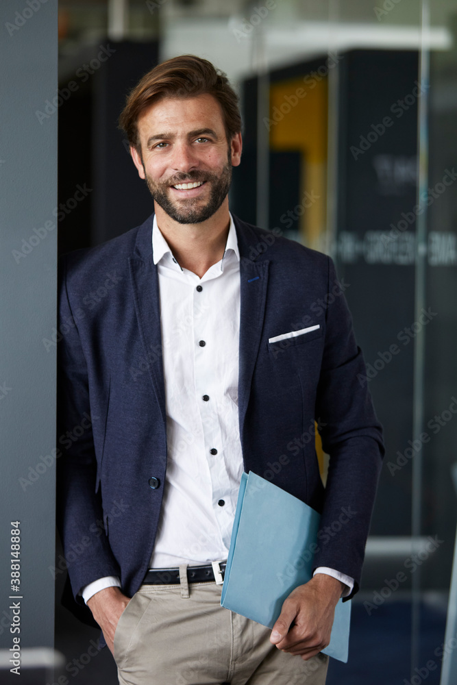 Smiling businessman holding document while standing at office Smiling businessman holding document while standing at office