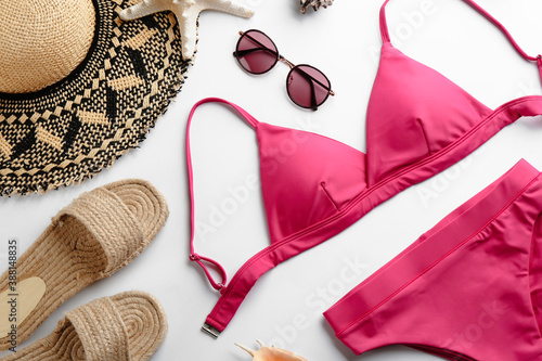 Beautiful pink bikini and beach accessories on white background, flat lay