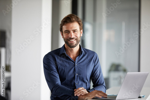 Smiling businessman using laptop while standing at desk in office photo