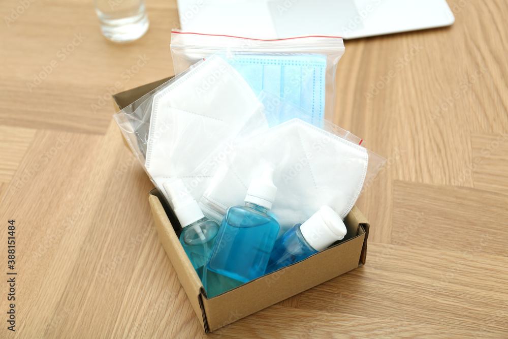 Cardboard box with antiseptics and respiratory masks on wooden table. Protective essentials during COVID-19 pandemic Cardboard box with antiseptics and respiratory masks on wooden table. Protective essentials during COVID-19 pandemic