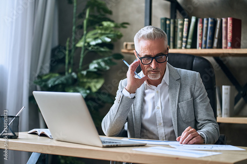 Mature man in glasses using laptop while working with report