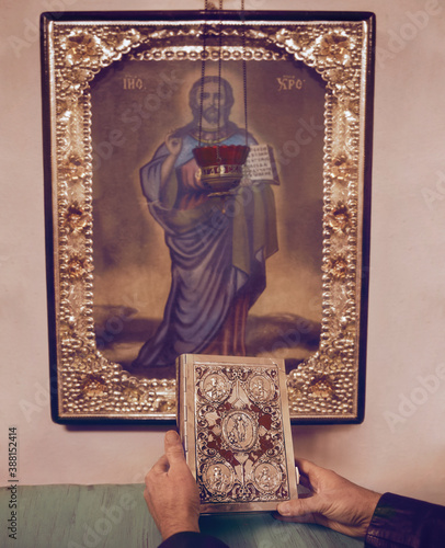 Bible in man’s hands in front of the icon of Jesus Christ. The Cathedral of the Nativity of the Blessed Virgin (1752-1763). Kozelets. Chernihiv Region. Ukraine. photo