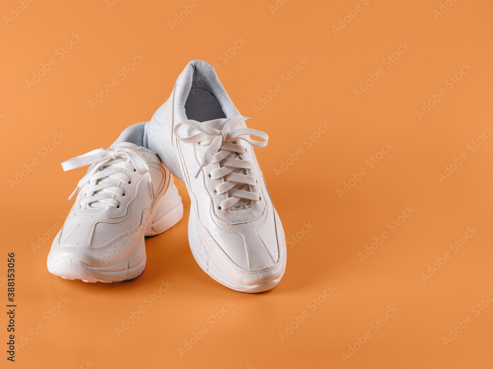 Pair of white tied laces sneakers over an orange background. New unisex chunky sole shoes for active lifestyle, fitness and sports. Copy space. Pair of white tied laces sneakers over an orange background. New unisex chunky sole shoes for active lifestyle, fitness and sports. Copy space.