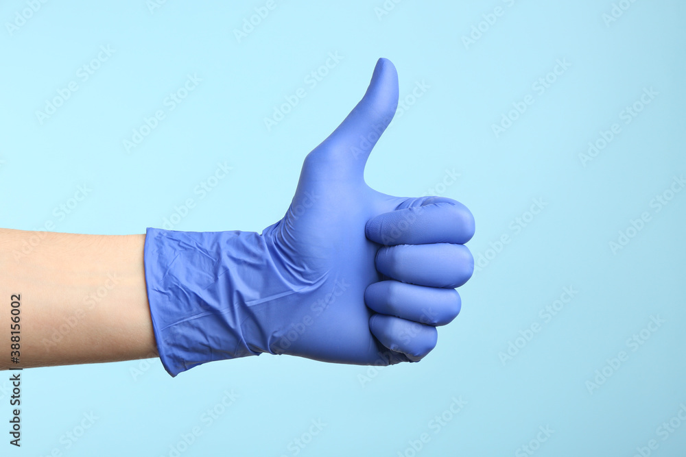 Person in medical gloves showing thumb up on light blue background, closeup of hand Person in medical gloves showing thumb up on light blue background, closeup of hand