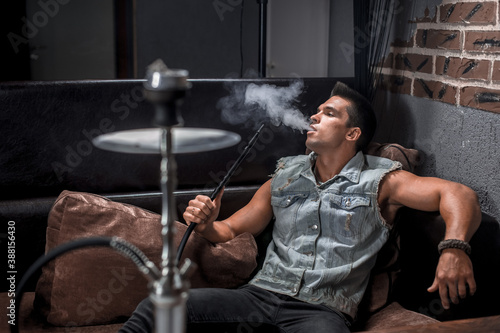 Young fellow relaxes in a hookah in nightclub.