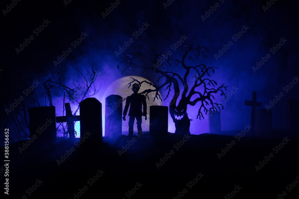 Naklejka premium Scary view of zombies at cemetery dead tree, moon, church and spooky cloudy sky with fog, Horror Halloween concept with glowing pumpkin. Selective focus