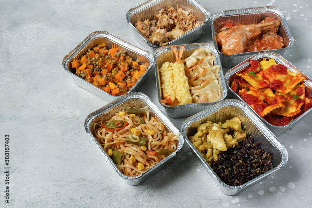 Food delivery. Different aluminium lunch box with ravioli, curry chicken  rice, gyoza tempura, noodles vegetables, lentils with pumpkin . airlines meals and snacks. takeaway takeout coronavirus food