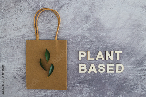 sustainable consumer choices, plant-based text with shopping bag and leaves on concrete background