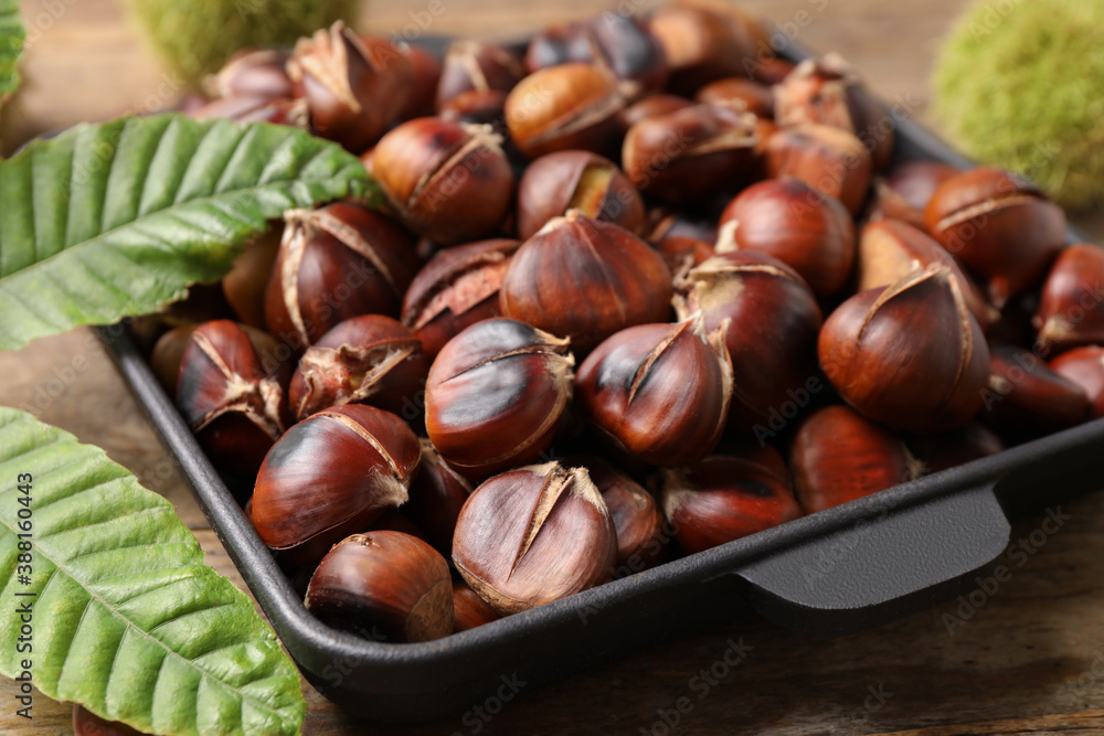 Delicious roasted edible chestnuts and green leaves on wooden table, closeup Delicious roasted edible chestnuts and green leaves on wooden table, closeup