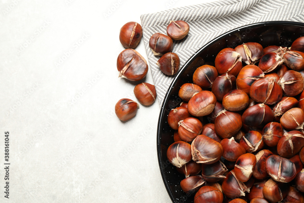Obraz premium Delicious roasted edible chestnuts on light grey table, flat lay. Space for text