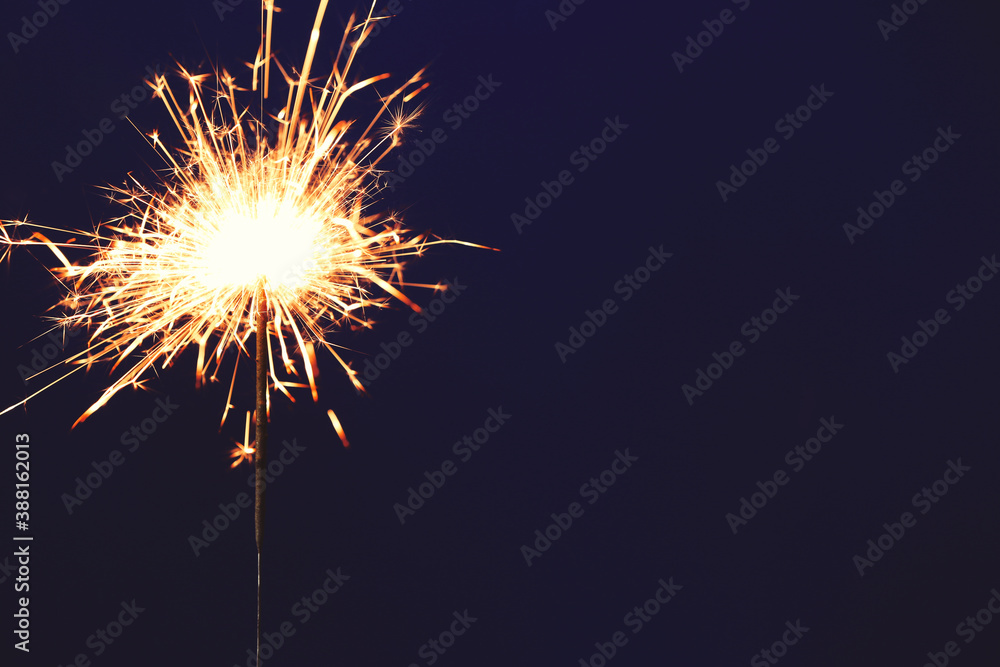 Bright burning sparkler on blue background, closeup. Space for text