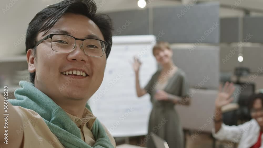 Close up of young Asian man standing in office with camera in his hands and making selfie with two his diverse coworkers Close up of young Asian man standing in office with camera in his hands and making selfie with two his diverse coworkers