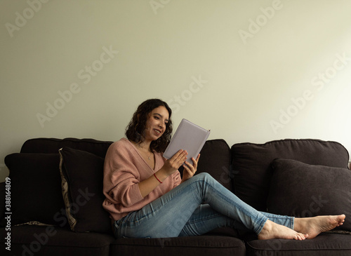 woman smiling with a pink sweater sitting on a black couch alone reading 