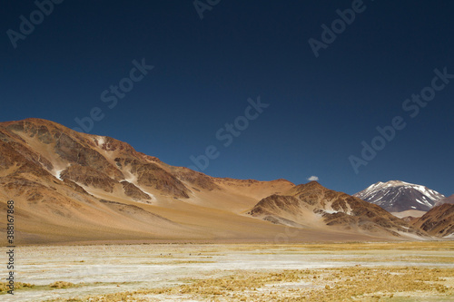 The Andes mountain range. Panorama view of the yellow meadow, brown mountains, golden valley and Volcano Incahuasi, under a deep blue sky.