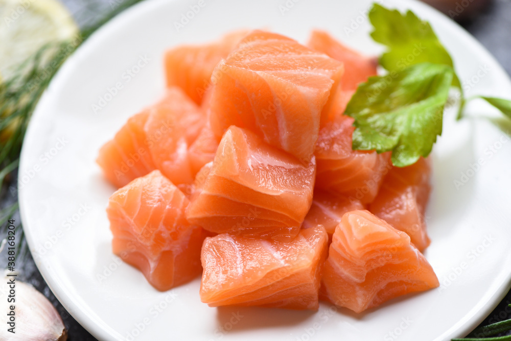 Raw salmon filet cube with herbs and spices on white plate on dark background