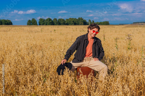 Wallpaper Mural Tall handsome man with black hat and pink sunglasses sitting on a brown at golden oat field. Torontodigital.ca