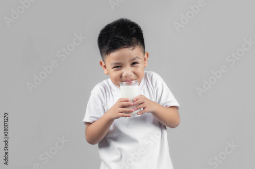 Asian child drinking milk from a glass on gray background