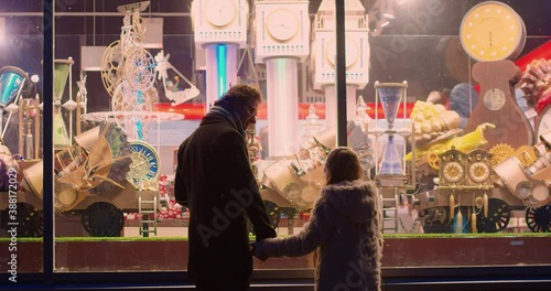 Father and daughter holding hands approach the window of toy store where amazing mechanisms move. Christmas fairy tale.