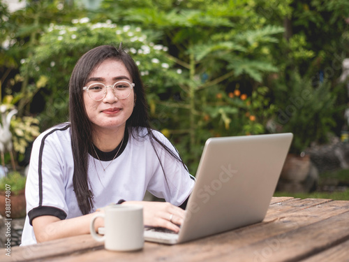 A young filipino woman with slight acne but very confident in herself. Outdoors on the bench with a laptop and a cup of coffee. Young entrepreneur concept photo