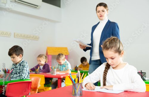 Cute intelligent preteen girl studying in classroom on background with classmates and teacher