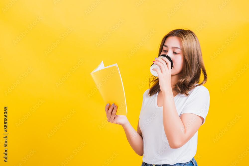 Portrait Asian Thai beautiful happy young woman standing holding drinking take away cup coffee paper and reading yellow book or diary, studio shot isolated on yellow background, with copy space Portrait Asian Thai beautiful happy young woman standing holding drinking take away cup coffee paper and reading yellow book or diary, studio shot isolated on yellow background, with copy space