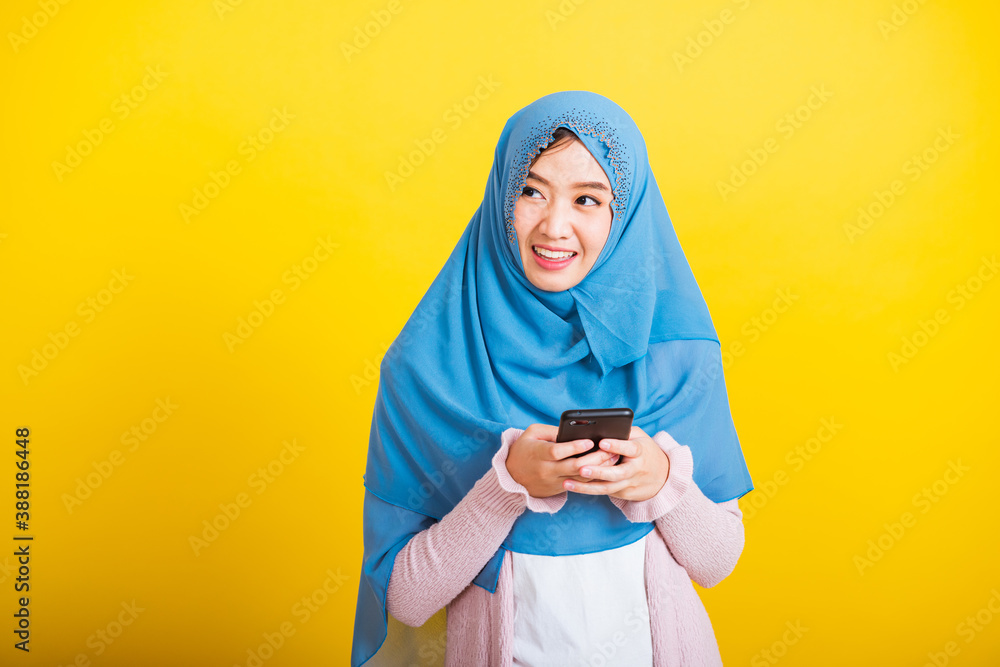 Asian Muslim Arab, Portrait of happy beautiful young woman Islam religious wear veil hijab funny smile she using hold mobile smart phone reading social media isolated on yellow background Asian Muslim Arab, Portrait of happy beautiful young woman Islam religious wear veil hijab funny smile she using hold mobile smart phone reading social media isolated on yellow background