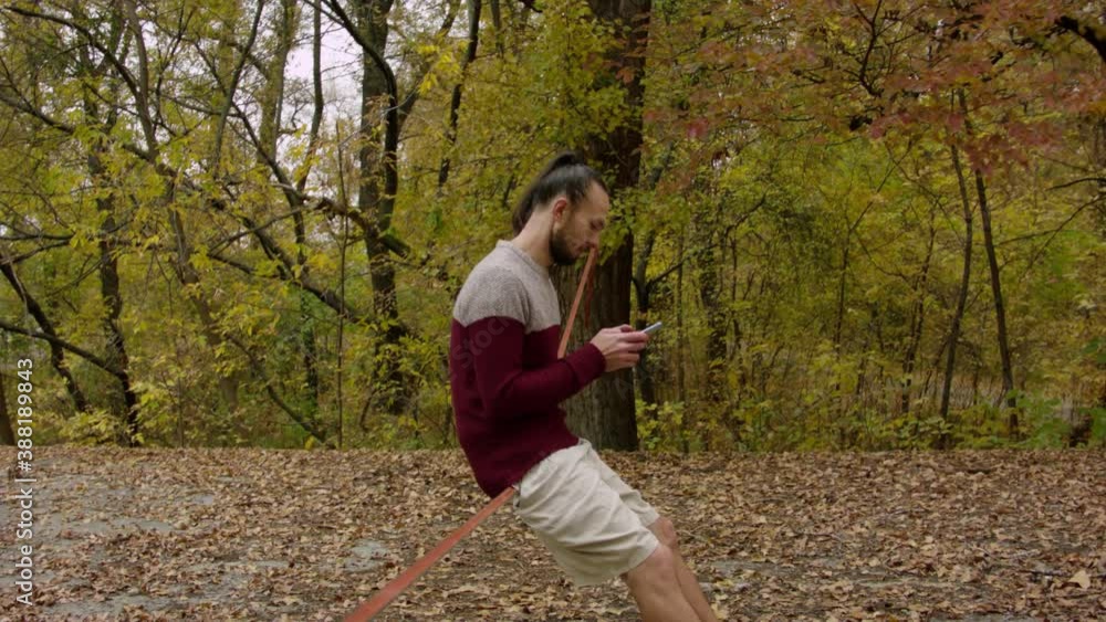 Caucasian man sets slackline between trees in the autumn forest. A man practices highlining in the autumn. Caucasian man sets slackline between trees in the autumn forest. A man practices highlining in the autumn.