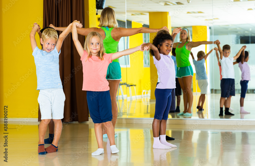 Group of children with their teacher holding hands and dancing in circle in dance school.