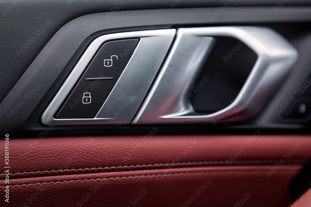 Сlose up of a door control panel  with chrome handle on the car door, common black and red genuine leather in a new car. Arm rest with   control buttons