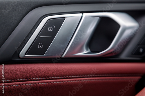 Сlose up of a door control panel  with chrome handle on the car door, common black and red genuine leather in a new car. Arm rest with   control buttons © Виталий Сова