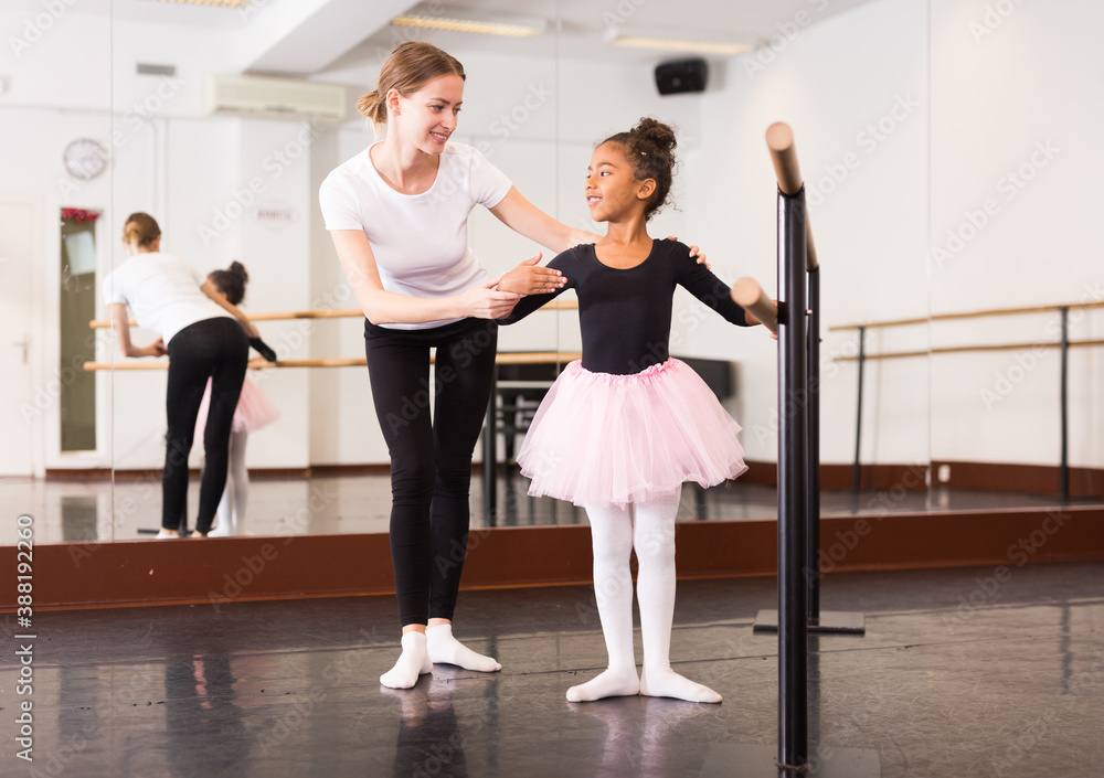 Fototapeta premium Little ballerina practicing choreographic elements with help of ballet teacher in dance hall