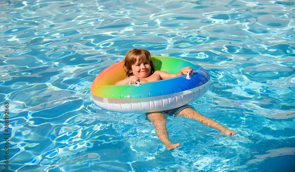Kid in swimming pool, relax swim on inflatable ring and has fun in water on summer vacation.