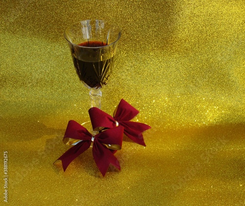 Copa de cristal con vino tinto sobre fondo dorado diamantado y dos moños aterciopelados en color guindo 5 photo