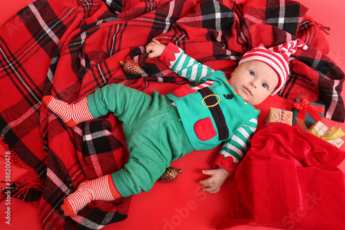 Cute little baby in elf's costume and with Christmas gifts on color background © Pixel-Shot
