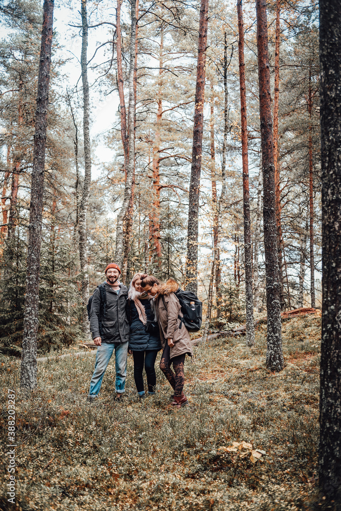 Fototapeta premium Cheerful and happy group of three tourists pose in autumn forest around trees and look at camera.