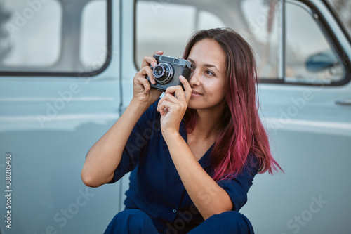 Beautiful female taking picture on street with photocamera. Blue car on background. New emotion and travel time concept