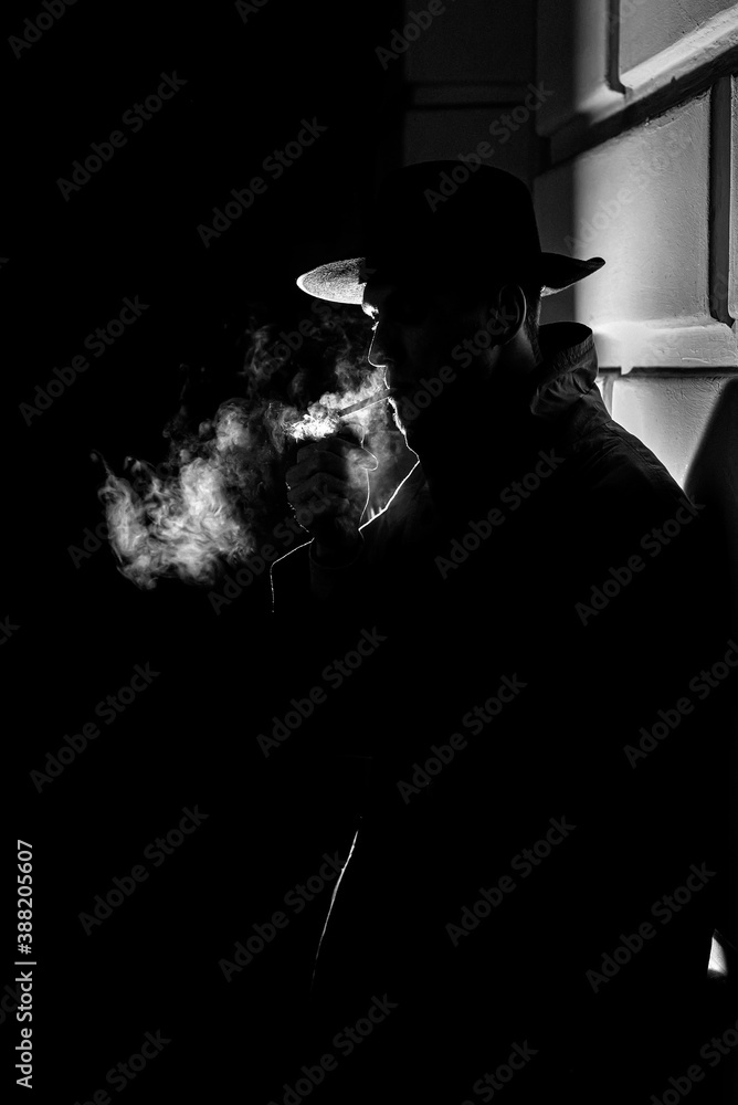 dark dramatic silhouette of a man in a hat Smoking a cigarette on the street at night