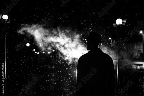 dark silhouette of a man in a hat in the rain on a night street in a city
