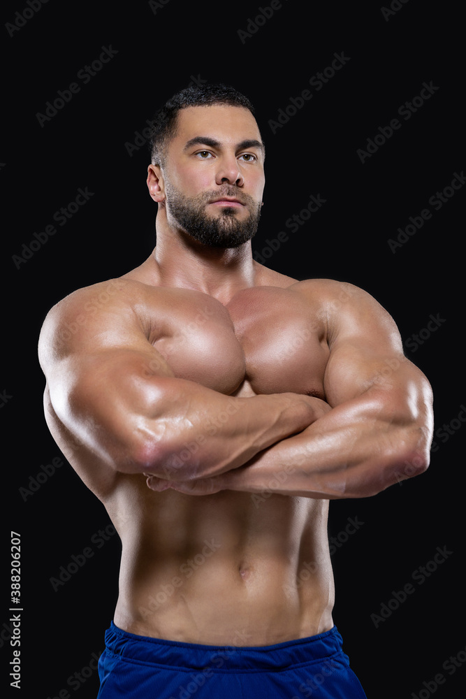 Strong athlete man is standing with hands folded on his chest looking at camera isolated on black background