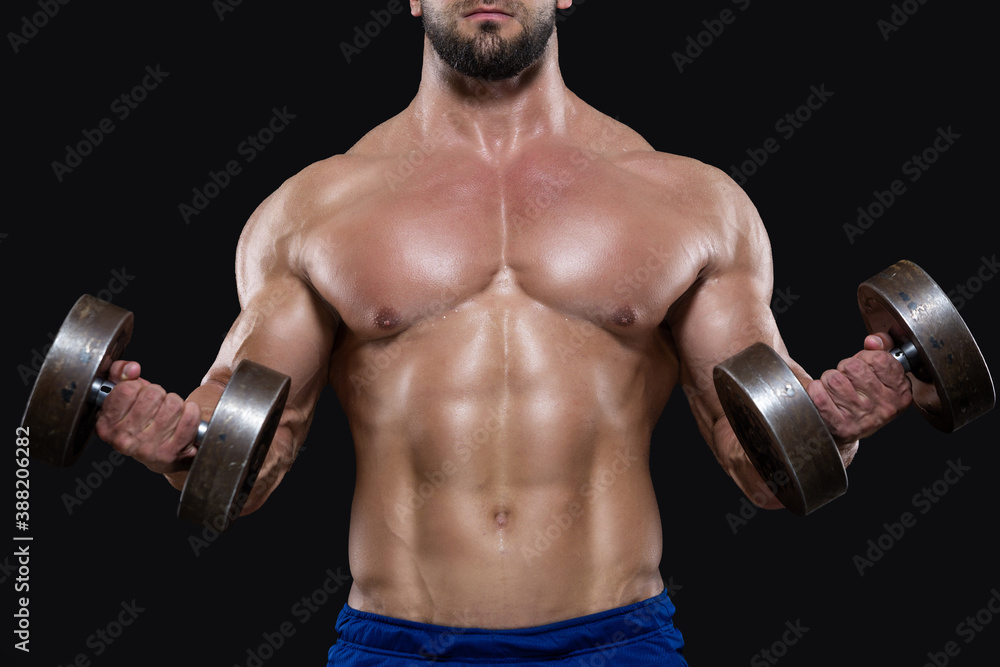 Close up of muscular sportsman lifting heavy dumbbells showing his strong biceps isolated on black backgrounds