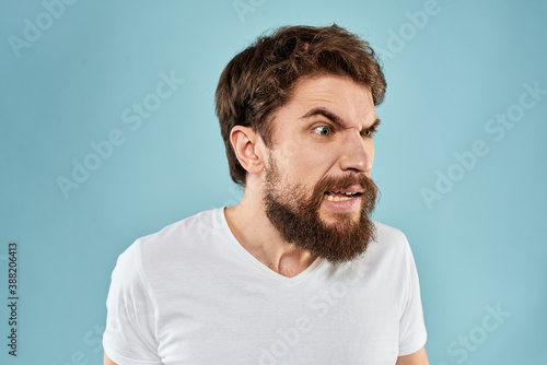 Bearded man in white T-shirt emotions gestures with hands displeased facial expression blue background