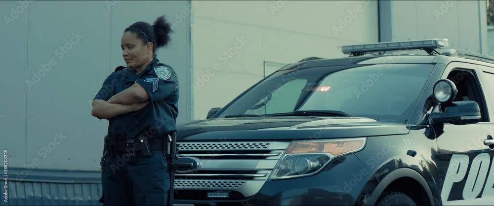 Mixed race female police officer posing against police car with flashing lights. Shot on RED cinema camera with 2x Anamorphic lens Mixed race female police officer posing against police car with flashing lights. Shot on RED cinema camera with 2x Anamorphic lens