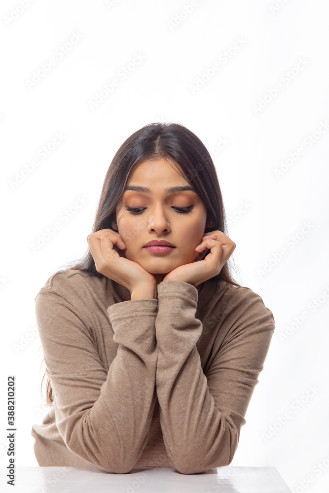 Young woman looking downwards with her face resting in her hands Young woman looking downwards with her face resting in her hands