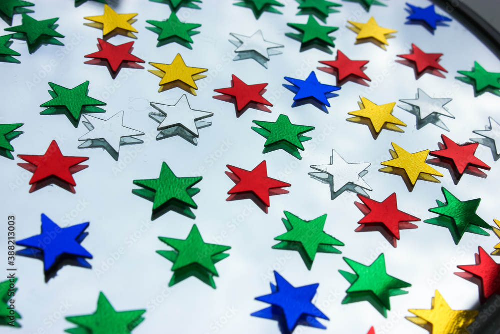 Confetti of colorful stars on the glass surface of the mirror, festive background
Confetti of colorful stars on the glass surface of the mirror, festive background