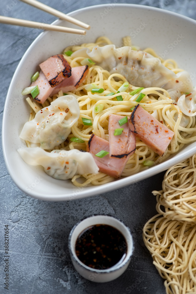 Asian dry wonton noodles or egg noodles served with wontons and chinese bbq pork slices, closeup, vertical shot