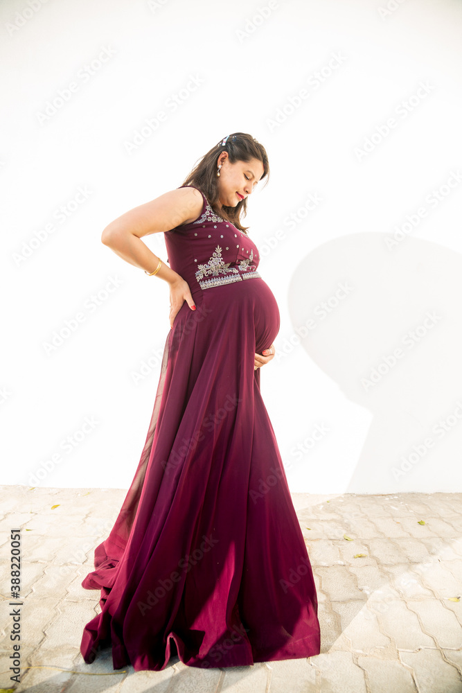 Young pregnant woman looking at belly standing against white background outdoor studio shot, happy female expecting baby, motherhood and pregnancy concept, copy space. Young pregnant woman looking at belly standing against white background outdoor studio shot, happy female expecting baby, motherhood and pregnancy concept, copy space.