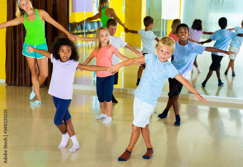 Group of glad positive smiling children practicing vigorous jive movements in dance class with female coach